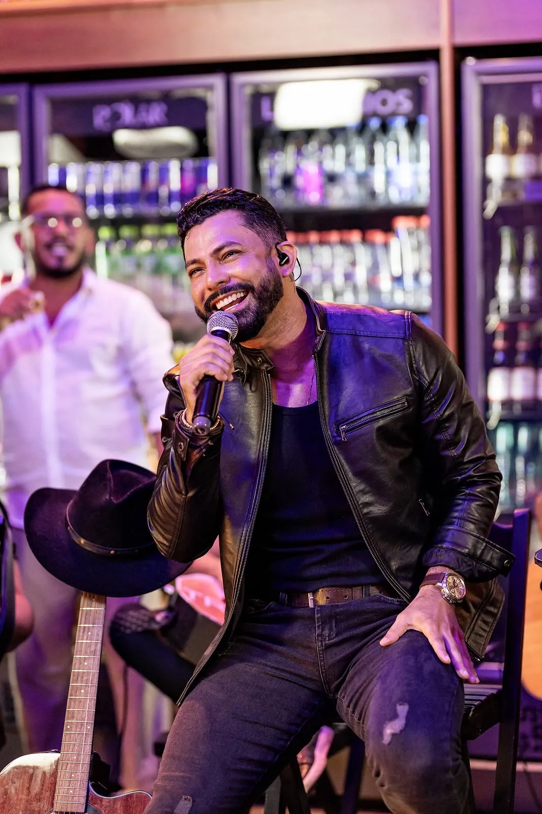 Lukas Santos rindo com o microfone, sentado no palco